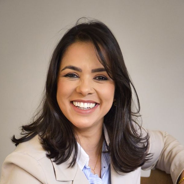 Advogada sorrindo, de blazer social claro, olhando para a câmera. Imagem ilustrativa.